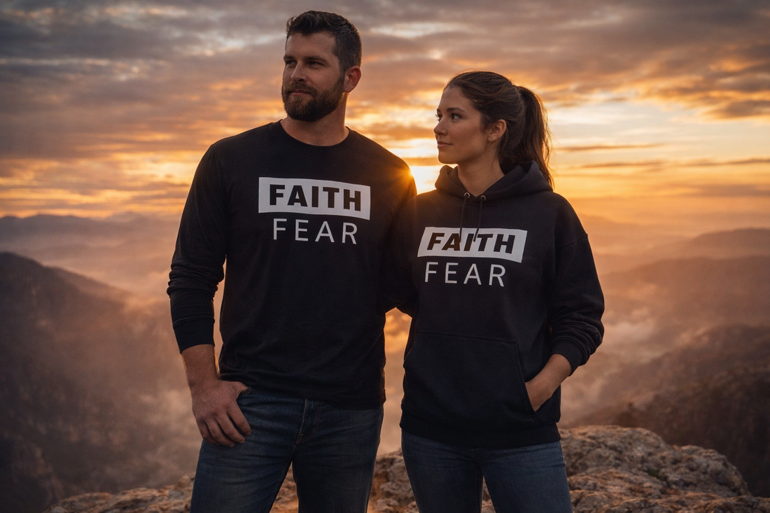 Rugged man in Faith Over Fear long sleeve shirt standing beside woman wearing Faith Over Fear hoodie on mountain overlook at sunrise representing Christian courage and faith.