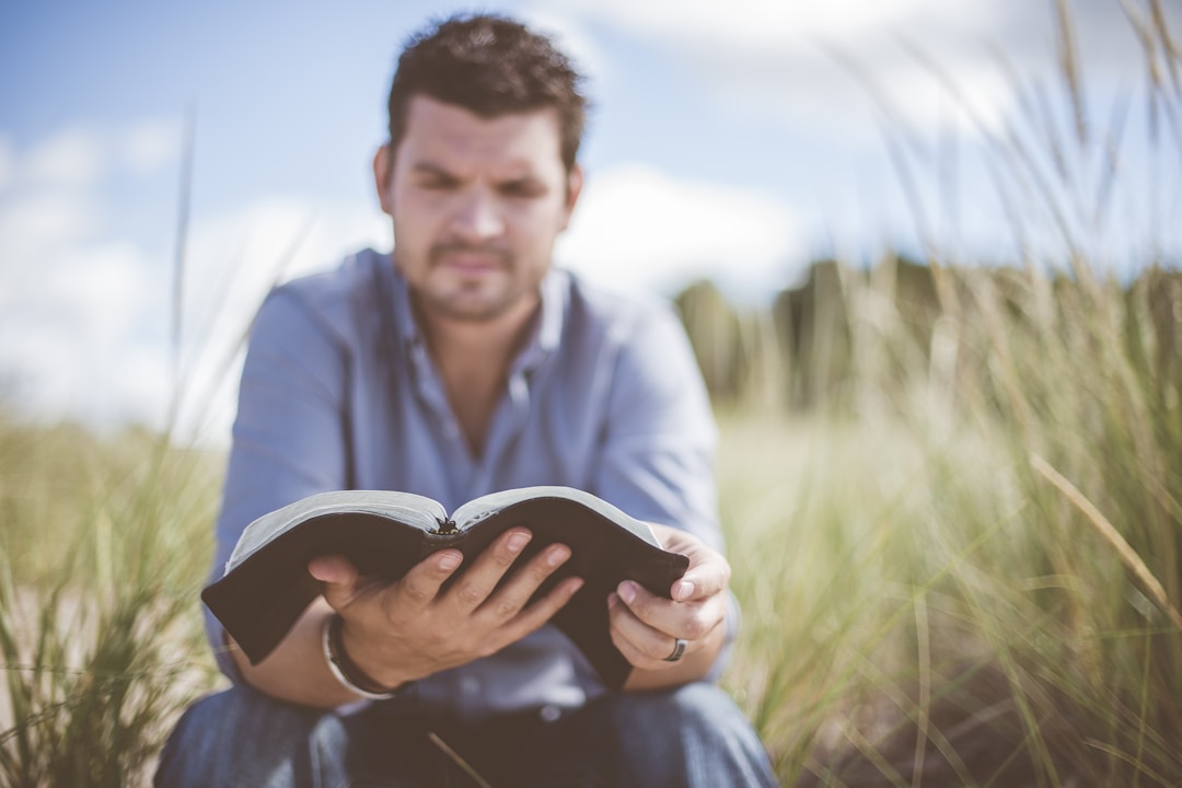 A man sitting in a grassy field, reading a book, representing personal spiritual growth.