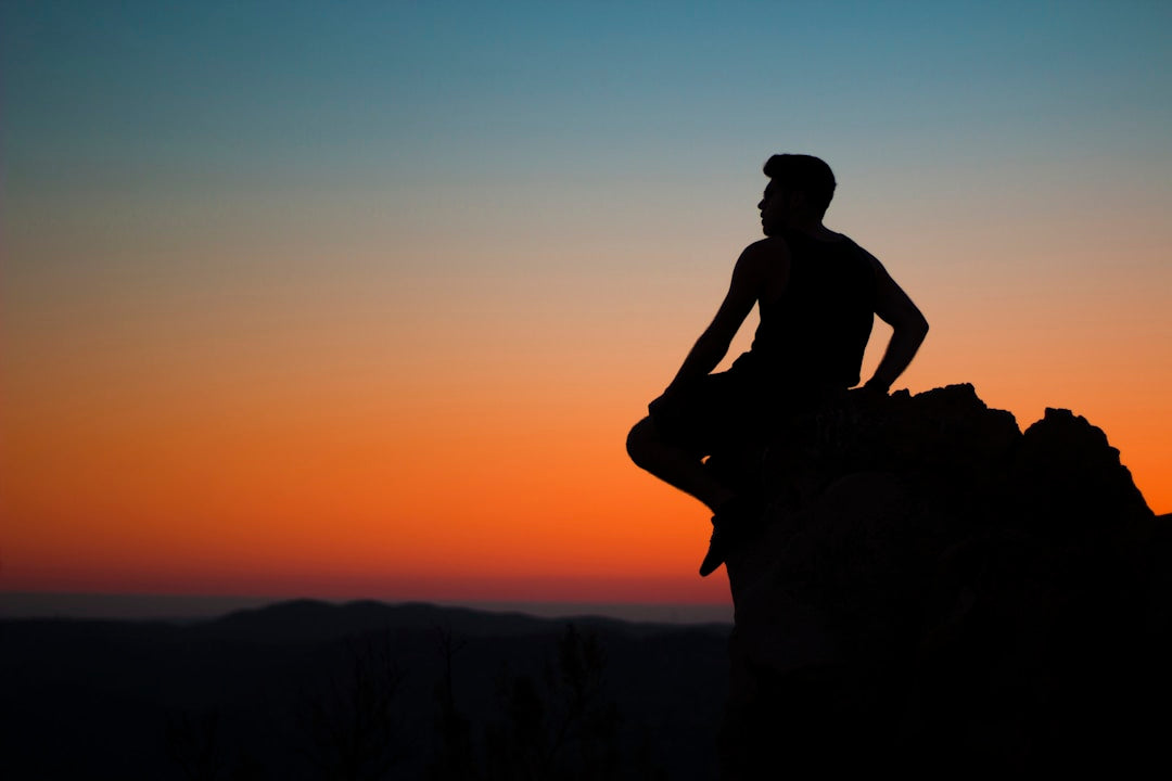 Silhouette of a man sitting on a mountain peak at sunrise, representing contemplation and active discipleship