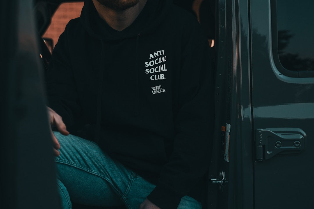 Man sitting in the back of a truck wearing a hoodie, looking contemplative and masculine