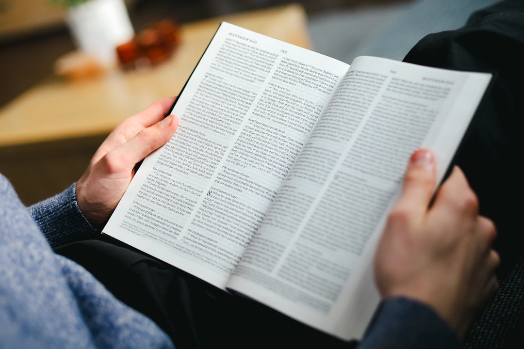 A man sitting on a couch, deeply focused on reading the Bible.