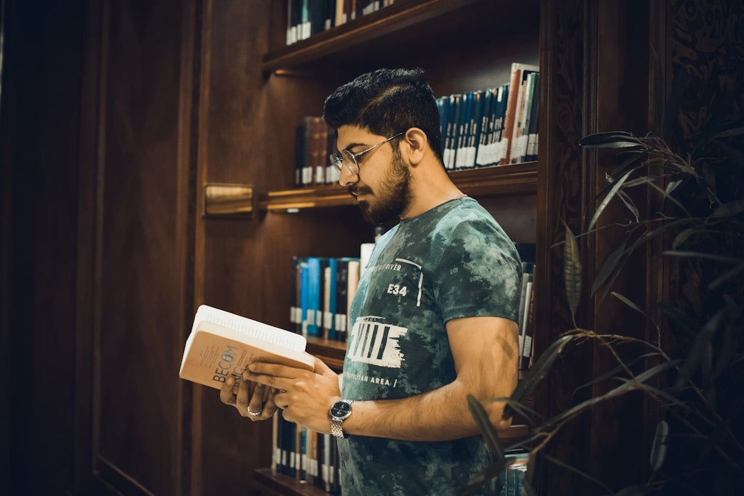 A man with a beard sitting in a library, intently reading a book, representing the study of biblical truth and wisdom.