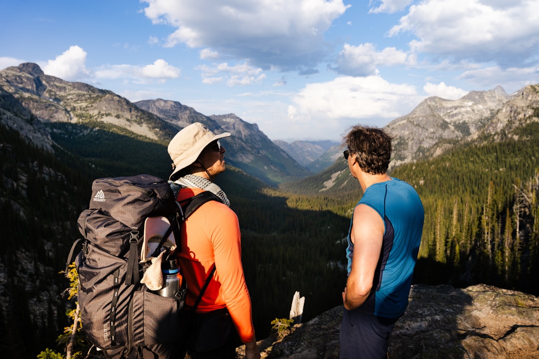 Two men standing on a mountain peak looking out at a scenic landscape, symbolizing mentorship and journey.
