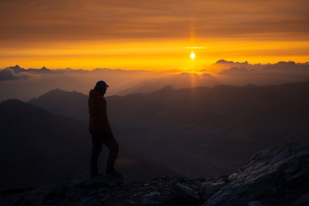 Man standing on a mountain peak at sunset, representing the journey of discipleship and spiritual strength.